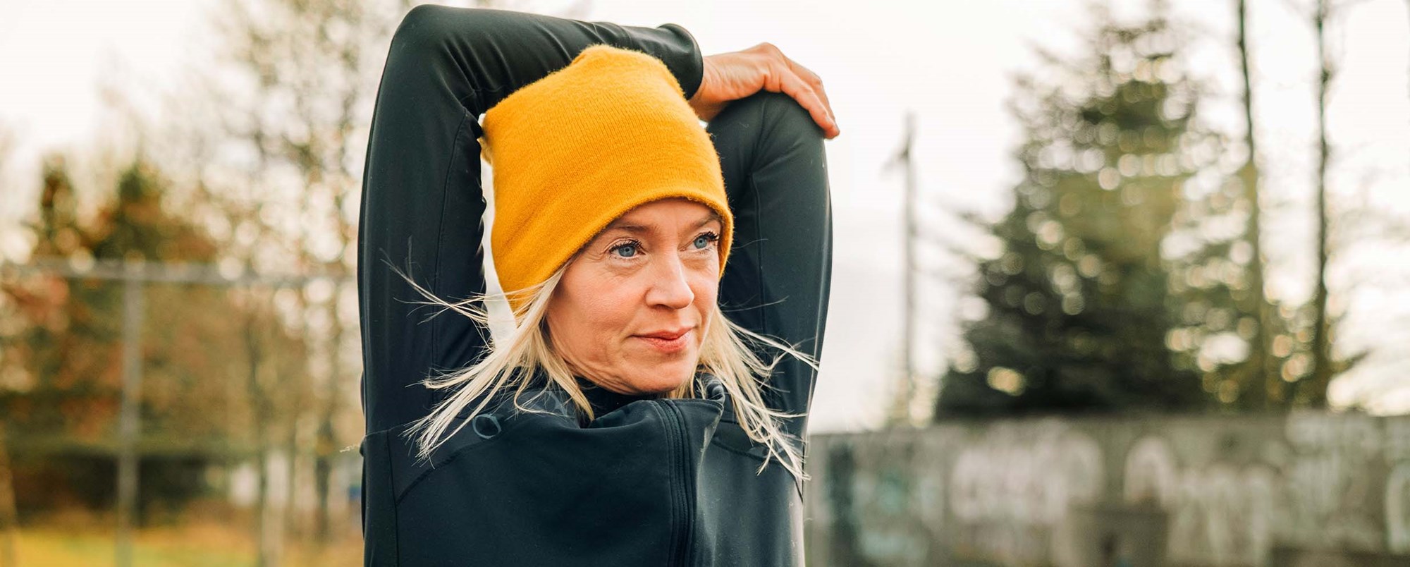 Kvinna i orange toppluva och svart tröja stretchar triceps