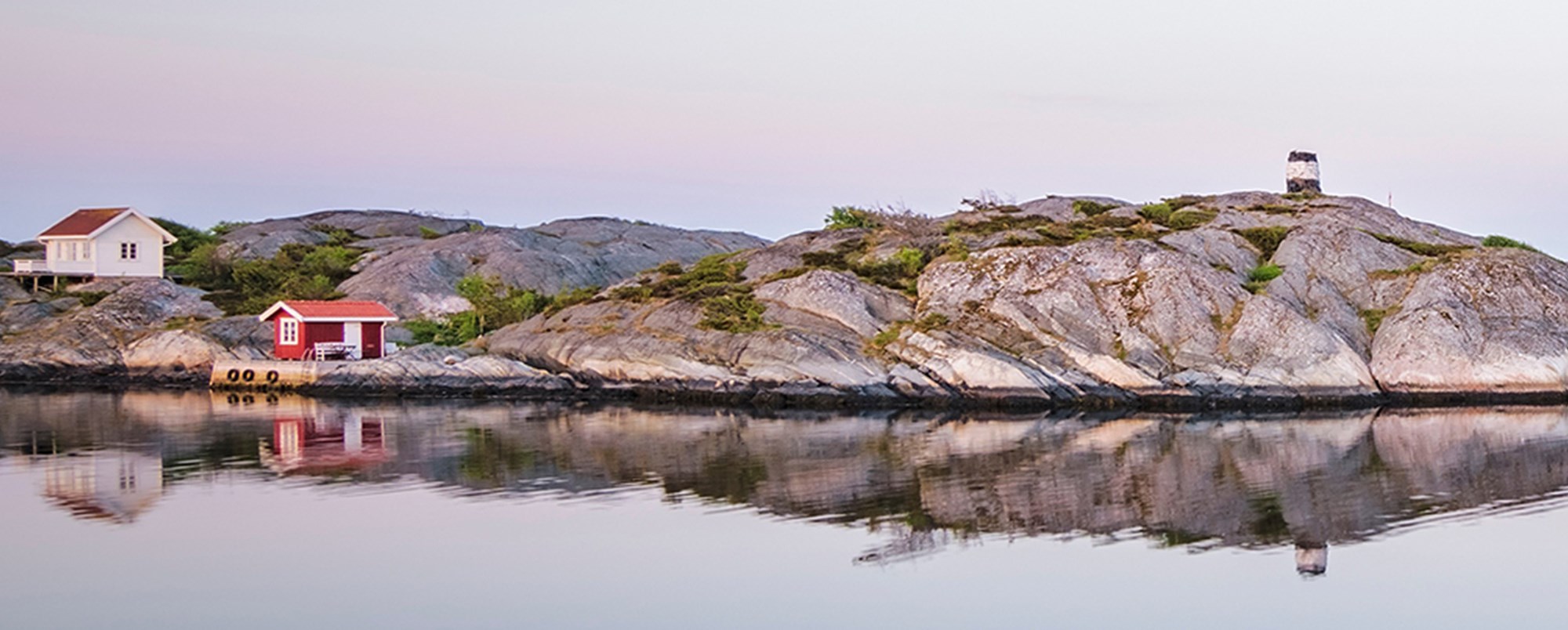 Skärgård, röd och vit stuga bland kobbar och vatten