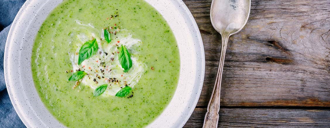 Grönsakssoppa med basilika i vit skål på träbord