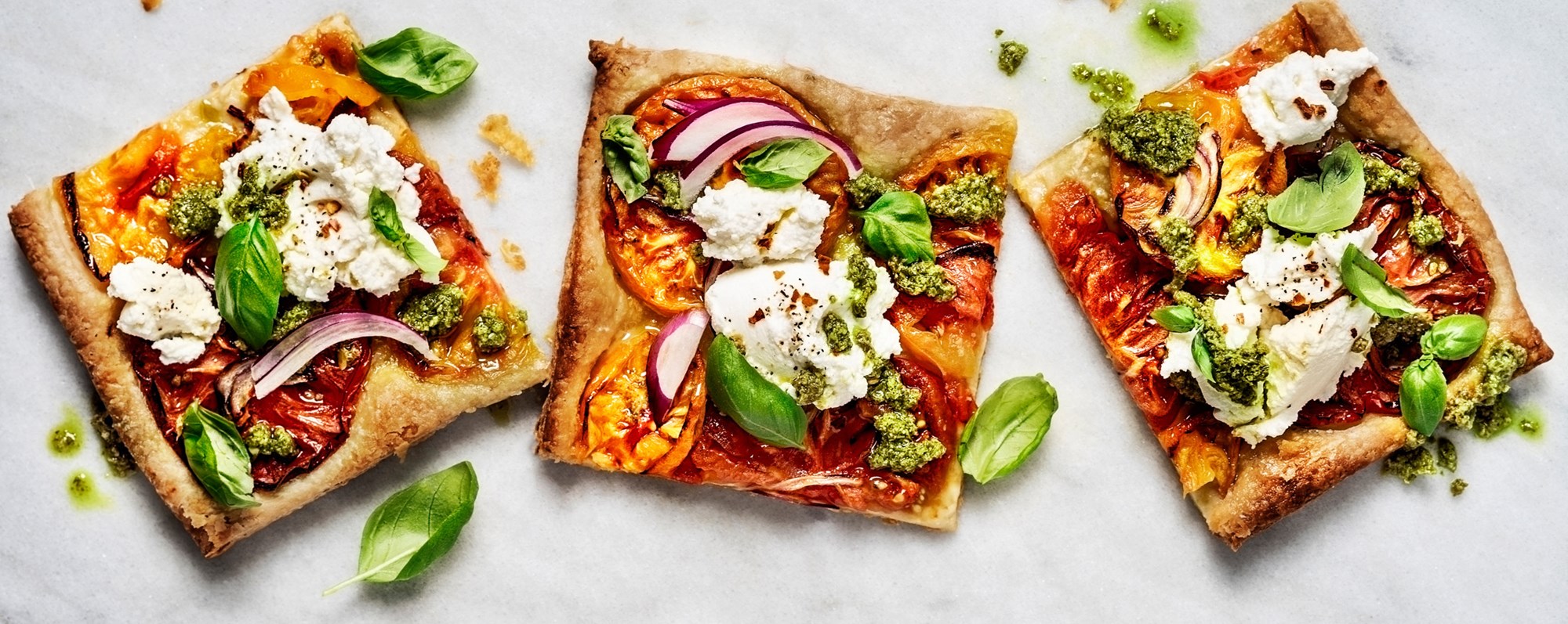 Tilltugg och dryck: Tre fyrkantiga pizzabitar med färskost basilika och tomat.