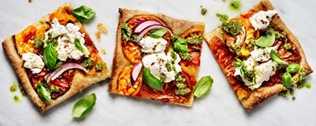 Tilltugg och dryck: Tre fyrkantiga pizzabitar med färskost basilika och tomat.