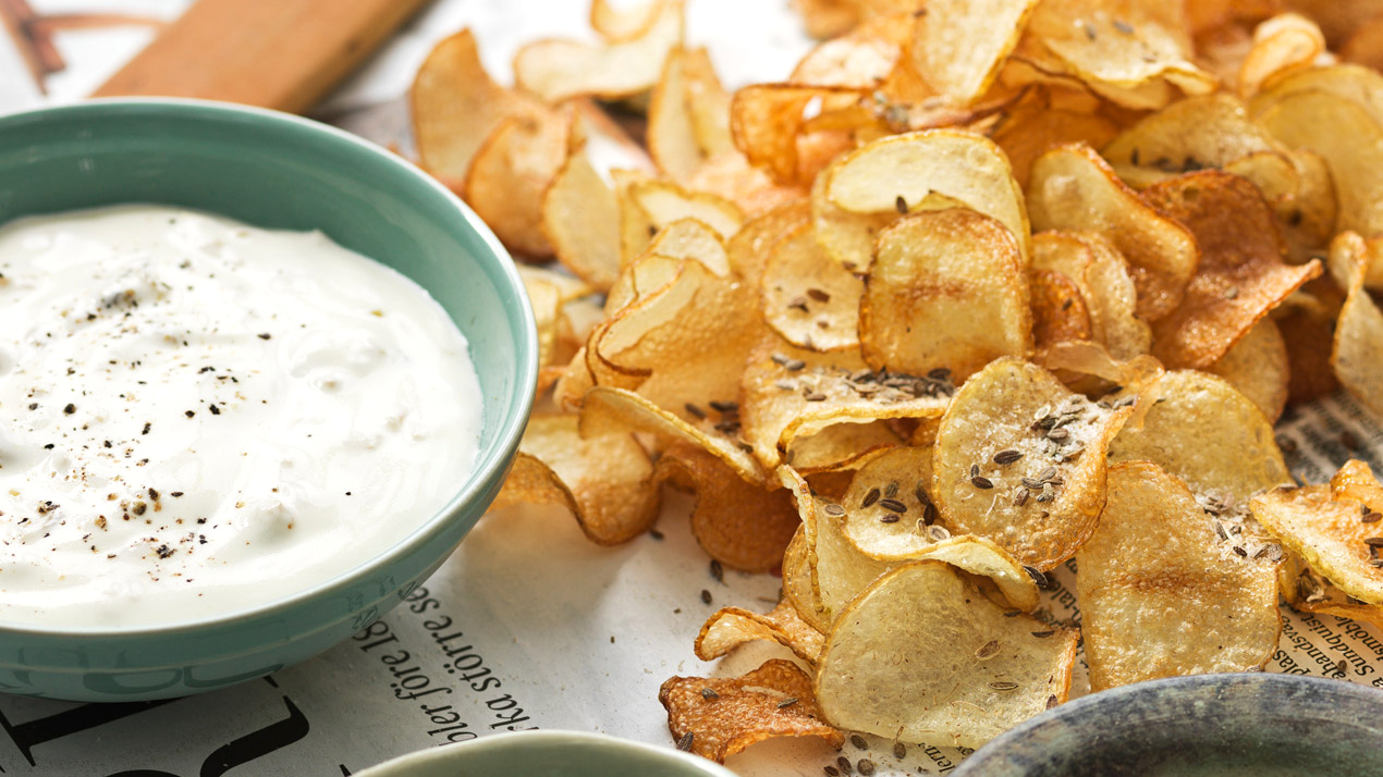 Bubblor och snacks: Sk&aring;l med dipp bredvid rustika chips p&aring; tidningspapper.
